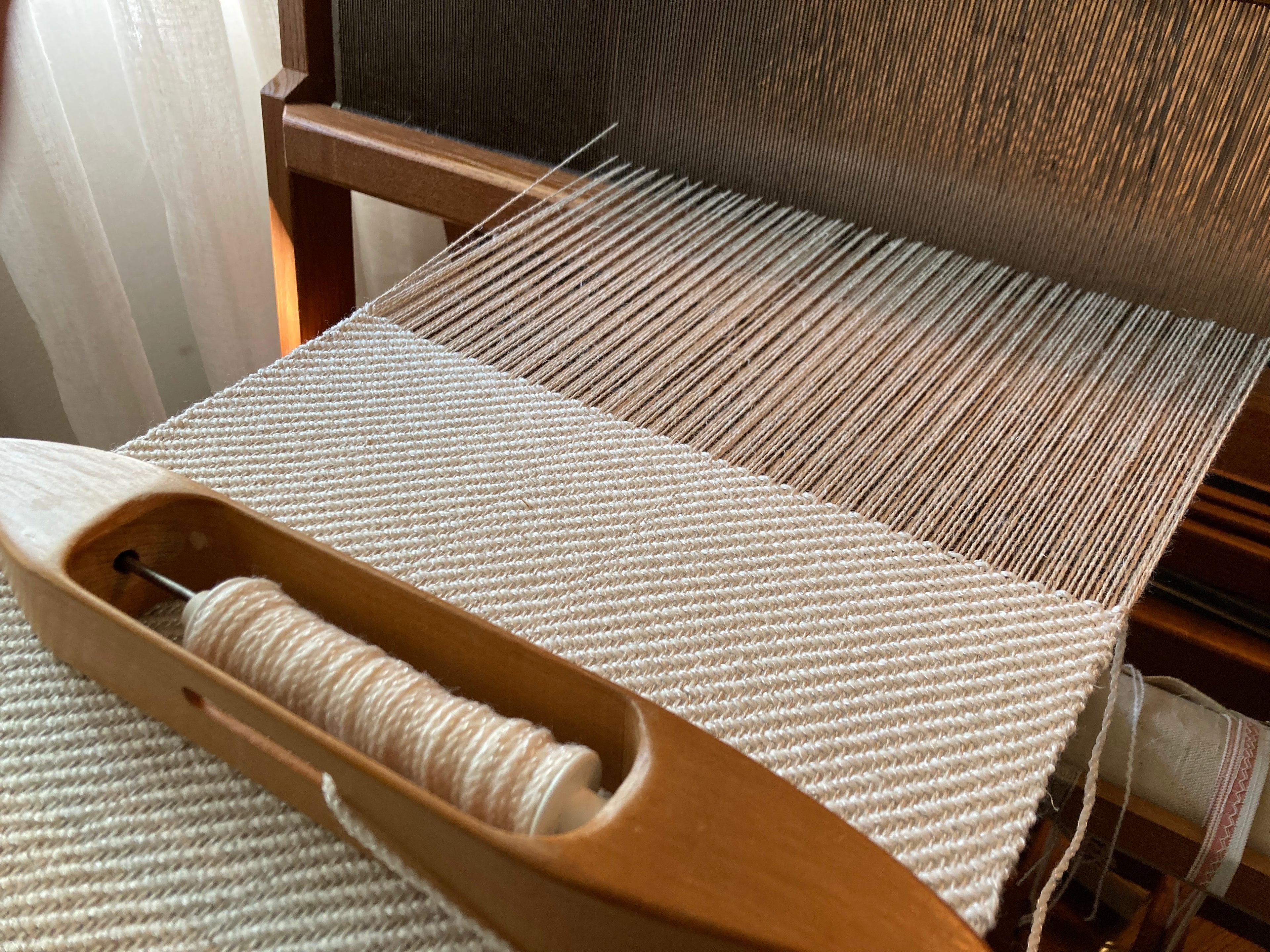 natural cream cloth being woven on a loom with shuttle in foreground